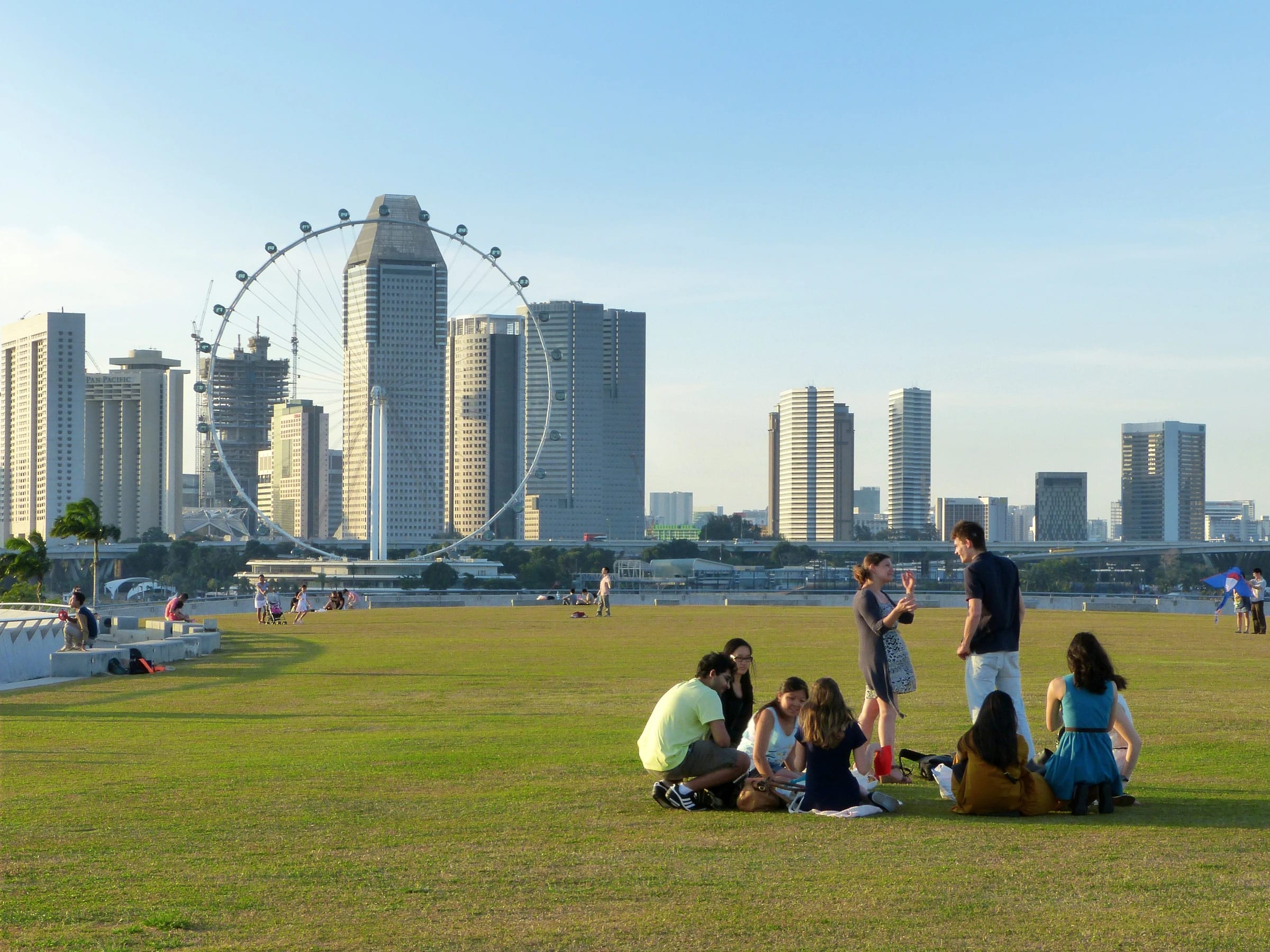 People sitting and standing on the rooftop lawn at Marina Barrage with the Singapore Flyer and skyline behind them.
